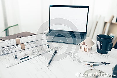 Mini model house, pencil, protractor, tape measure, compass, laptop and roll blueprint plan on workplace. Architect and engineer Stock Photo