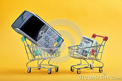 Mini shopping cart with bank cards inside, dollar banknotes and terminal on yellow background. Trolley and money Stock Photo