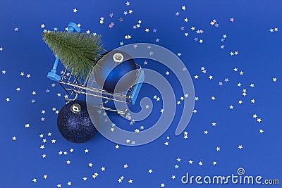 Mini shopping cart with small Christmas tree and navy Christmas decoration bauble balls on blue background with silver Stock Photo