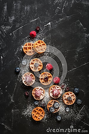 Mini waffles with raspberries and blueberries on a black stone background, flat lay. Belgian traditional waffles with berries. Top Stock Photo