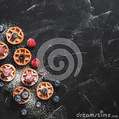 Mini waffles with raspberries and blueberries on a black stone background, flat lay. Belgian traditional waffles with berries. Top Stock Photo