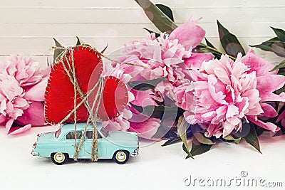 Miniature blue toy car carrying a heart and pink peonies on the Stock Photo