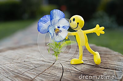 Miniature bright toy figure of a yellow cheerful little people near a pansy flower. concept of love, joy, happiness Stock Photo