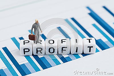 Miniature businessman in suit walking on cube block with alphabets building the word Profit on blue yearly bar chart report, Stock Photo