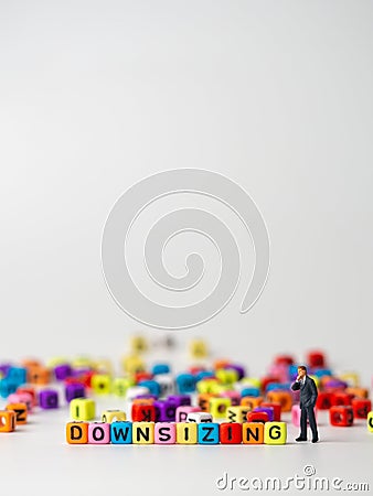 Miniature figure businessman in dark blue suit standing backside of colorful of downsizing alphabet and thinking abount how to Red Stock Photo
