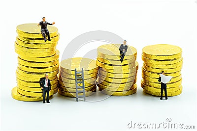 Miniature figure a group of business men sitting on top of pile stack of golden coins and some standing reading newspaper and Stock Photo