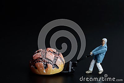 Miniature figurine of a man transporting a giant loaf of bread with a cart Stock Photo