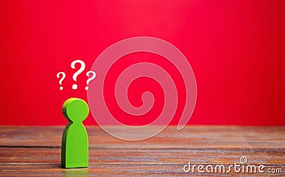 A miniature green man and question marks above him. Uncertainty. Search for an answer to a question. Problems and solutions Stock Photo