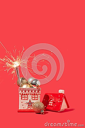 Miniature house with shiny golden Christmas balls and sparklers on red background. New Year or Christmas glowing decoration idea Stock Photo