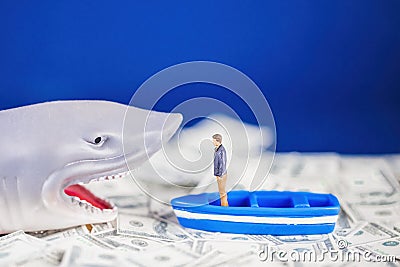 Miniature man on a small blue boat facing a loan shark on the dollar ocean. Loan shark concept Stock Photo