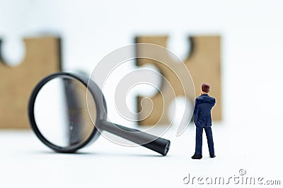 Miniature people : Businessman looking at jigsaw pieces through a magnifying glass. Image use for solve, solution, business Stock Photo