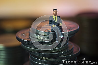 Miniature people Businessman sitting on coin stack warm background. Success Concept. Macro Stock Photo