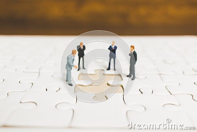 Miniature people: Businessman standing on jigsaw Stock Photo