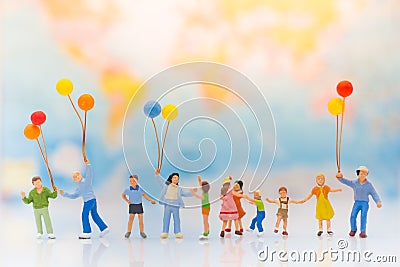 Miniature people: children hold balloons, and play together, background is map of world, Stock Photo