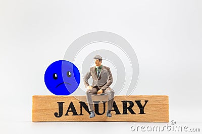Miniature people, A dejected businessman is sitting on a wooden with Blue face emoji , Blue monday concept Stock Photo