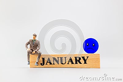 Miniature people, A dejected businessman is sitting on a wooden with Blue face emoji , Blue monday concept Stock Photo