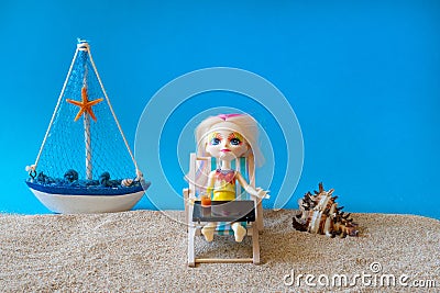 Miniature people girl with pink hair sits in a deck chair with a laptop and a glass of drink in her hands and looks at the sea. Stock Photo