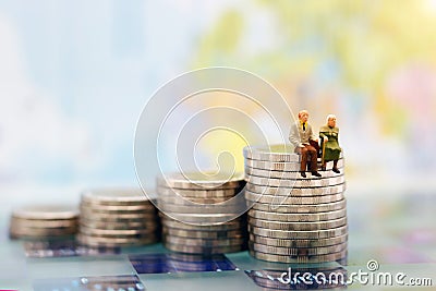 Miniature people: Happy senior couple sitting on coins stack Stock Photo