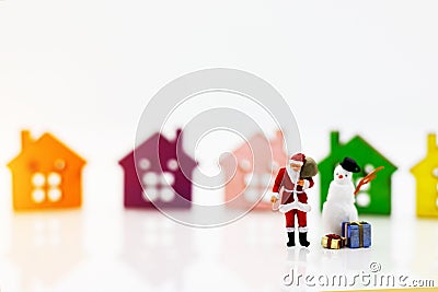 Miniature people: Santa Claus and snowman with gift standing before Wooden house model. Merry Christmas and Happy New Year concep Stock Photo