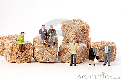 Miniature people: seniors, in front, cubes of brown sugar. Stock Photo