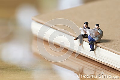 Miniature 2 people sitting Read newspaper on Note book using as background business concept Stock Photo