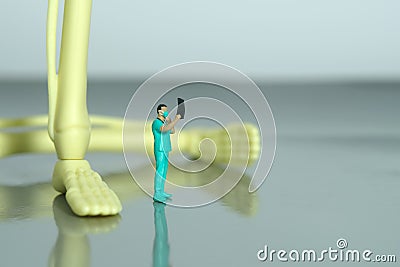 Miniature people toy figure photography. A doctor nurse looking on x ray result scan film in front of leg bone skeleton Stock Photo