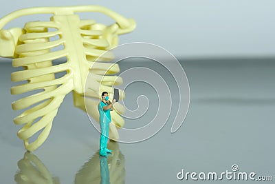 Miniature people toy figure photography. A doctor nurse observing on x ray result scan film in front of rib bone skeleton Stock Photo