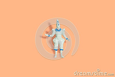 Miniature people toy figure photography. Full body of a white clown wearing cone hat. Isolate on orange pastel background Stock Photo