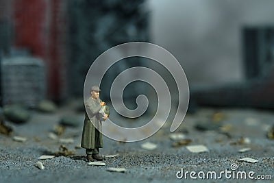 Miniature people toy figure photography. A military mail officer holding news pack envelope standing in the middle of ruined Stock Photo