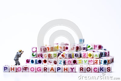 Miniature Photographer taking pictures before a Group Of Letters forming Words Spelling Stock Photo