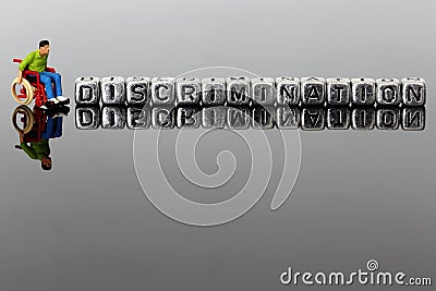 Miniature scale model man in a wheelchair with the word discrimination on beads Stock Photo
