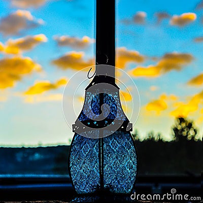 Miniature sky blue glass lantern lamp bauble against yellow orange southwest sunset glowing clouds Stock Photo