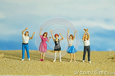 Miniature tiny people toys photography. Group of teens raised hand or hands up celebration at the beach Stock Photo