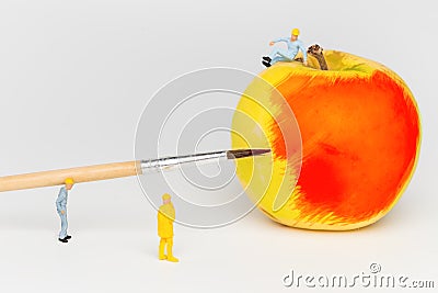 Miniature toy workers paint the apple. Stock Photo