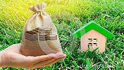 Miniature wooden house and money bag on grass. Real estate concept. Eco-friendly and energy efficient house. Buying a home outside Stock Photo