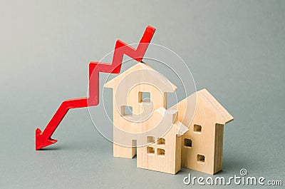 Miniature wooden houses and a red arrow down. The concept of low cost real estate. Lower mortgage interest rates. Falling prices Stock Photo
