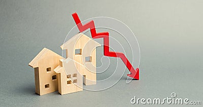 Miniature wooden houses and a red arrow down. The concept of low cost real estate. Lower mortgage interest rates. Falling prices Stock Photo