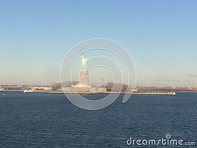 Minimal seascape view of the Statue of Liberty silhouette in the horizon, wide blue and yellow foggy sky in background, Staten Stock Photo