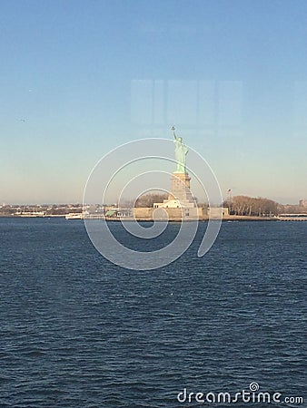 Minimal seascape view of the Statue of Liberty silhouette in the horizon, wide blue and yellow foggy sky in background, Staten Stock Photo