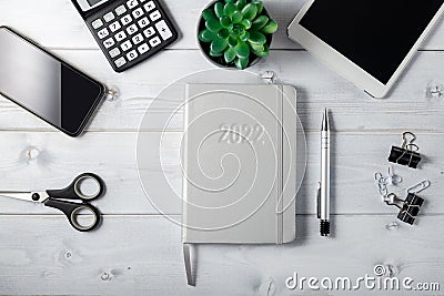 Minimal unisex workplace with tablet, silver notepad diary 2022, smartphone, small succulent and stationery on a light wooden Stock Photo