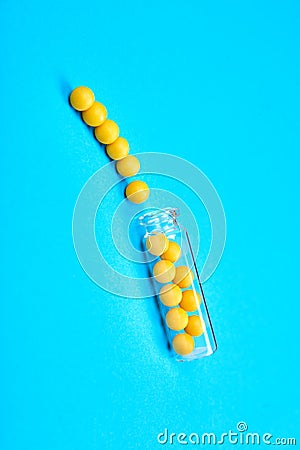 Minimalism style template for medical blog. Small glass bottle fwith small yellow pills spilled out blue background. Stock Photo