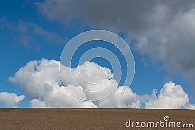 Minimalistic landscape with plowed soil and blue sky with big fluffy clouds Stock Photo