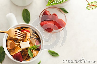 Minipancakes breakfast - white bowl with strawberries and pancakes, mik jar, honey, fresh mint and house plant. Lifestyle morning Stock Photo