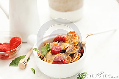 Minipancakes breakfast - white bowl with strawberries and pancakes, mik jar, honey, fresh mint and house plant. Lifestyle morning Stock Photo