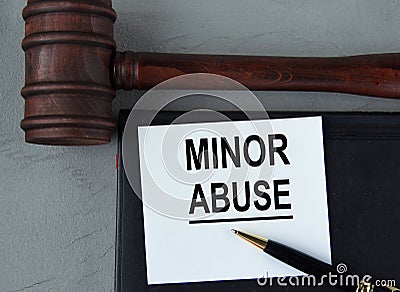 MINOR ABUSE - words on a white sheet with leather notebooks, a judge's hammer and a pen Stock Photo