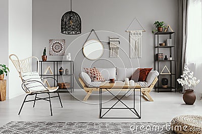 Mirror, macrame and graphic on the grey wall of warm ethno living room Stock Photo