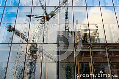 Mirror reflection of construction cranes appearing in the glass of a building near construction site Stock Photo