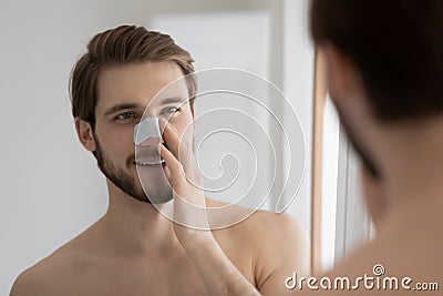 Mirror reflection smiling man applying anti blackhead mask on nose Stock Photo