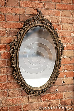 A mirror in a vintage openwork frame hangs on an old brick wall Stock Photo