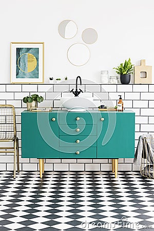 Mirrors and poster above green cabinet in bathroom interior with gold chair and plants. Real photo Stock Photo